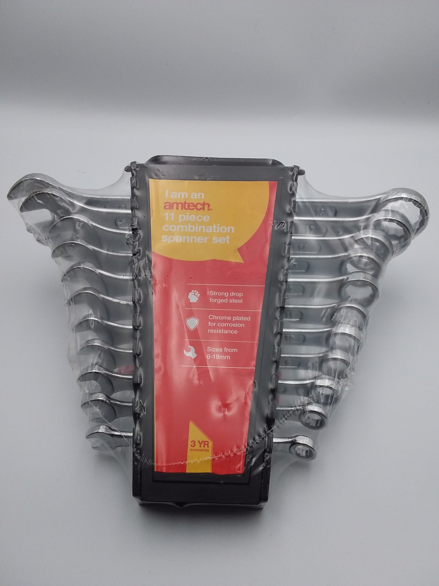 A set of silver combination spanners of various sizes, packaged in a black plastic case with a red and yellow label.