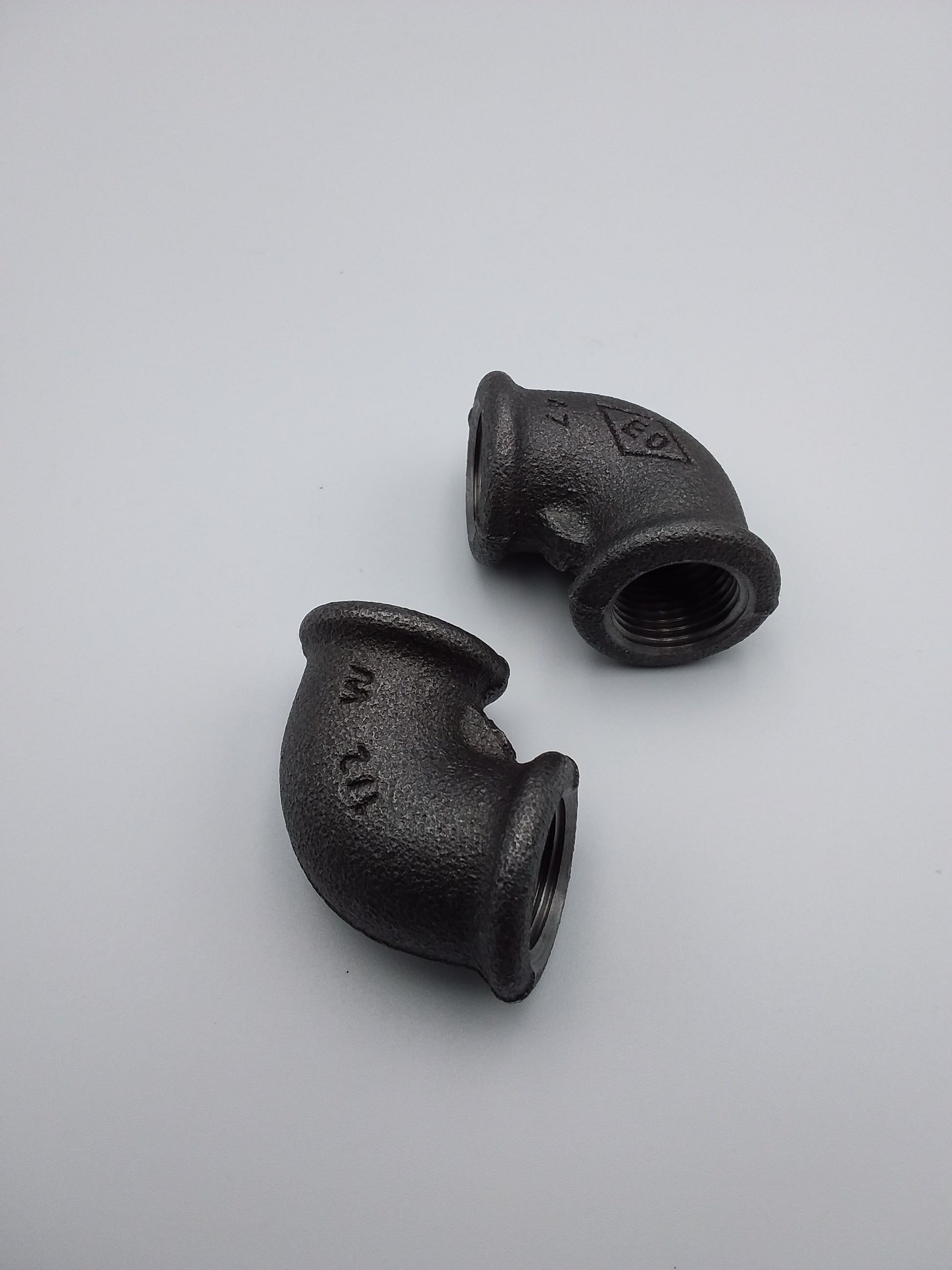 Black iron elbows, plumbing fixtures, placed on a light background.