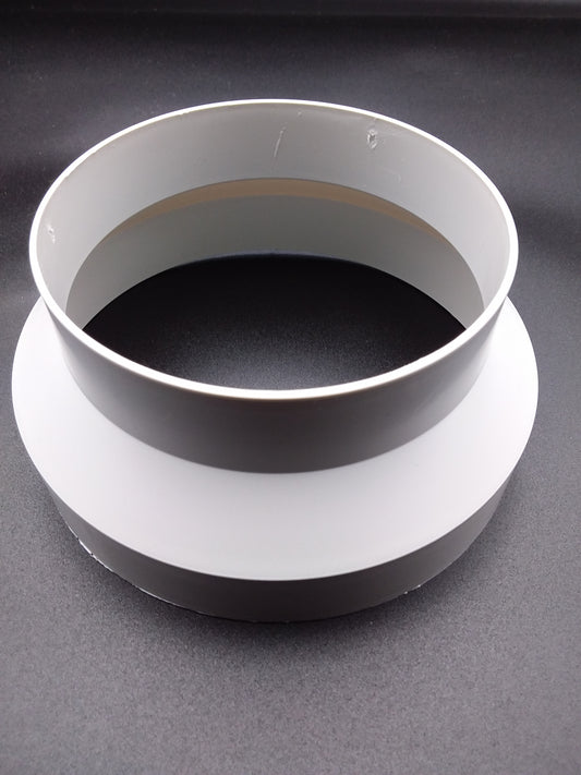 A white ducting reducer, with a round shape and two concentric rings, placed on a flat surface.