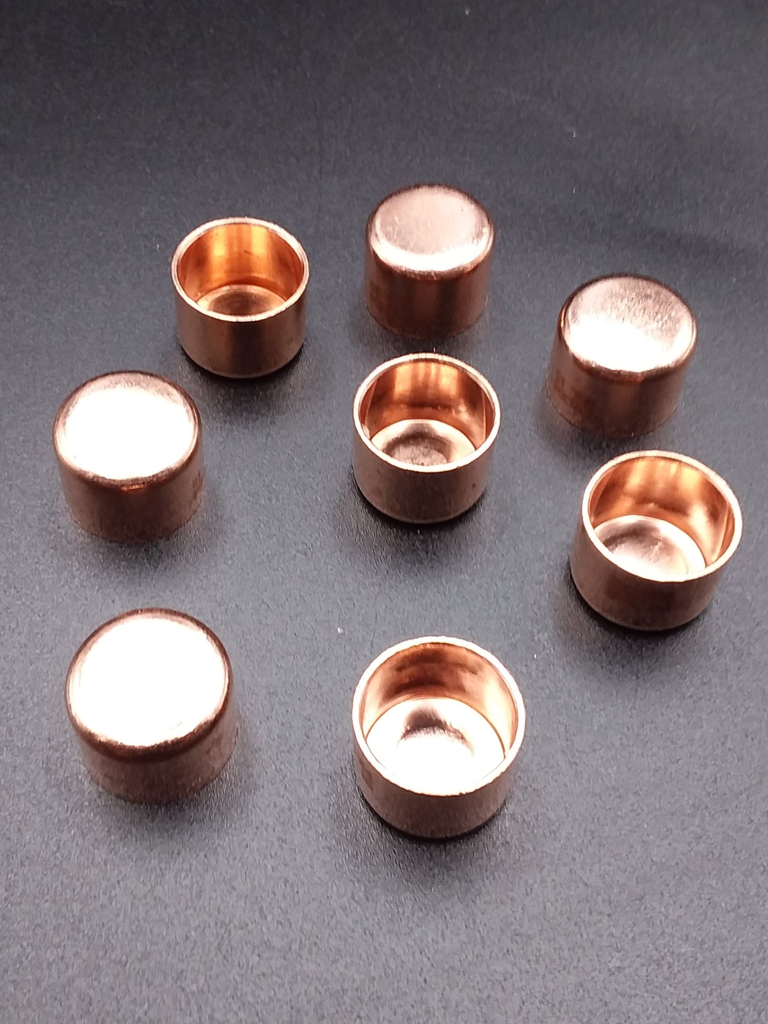 Copper endfeed pipe caps scattered on a dark surface.