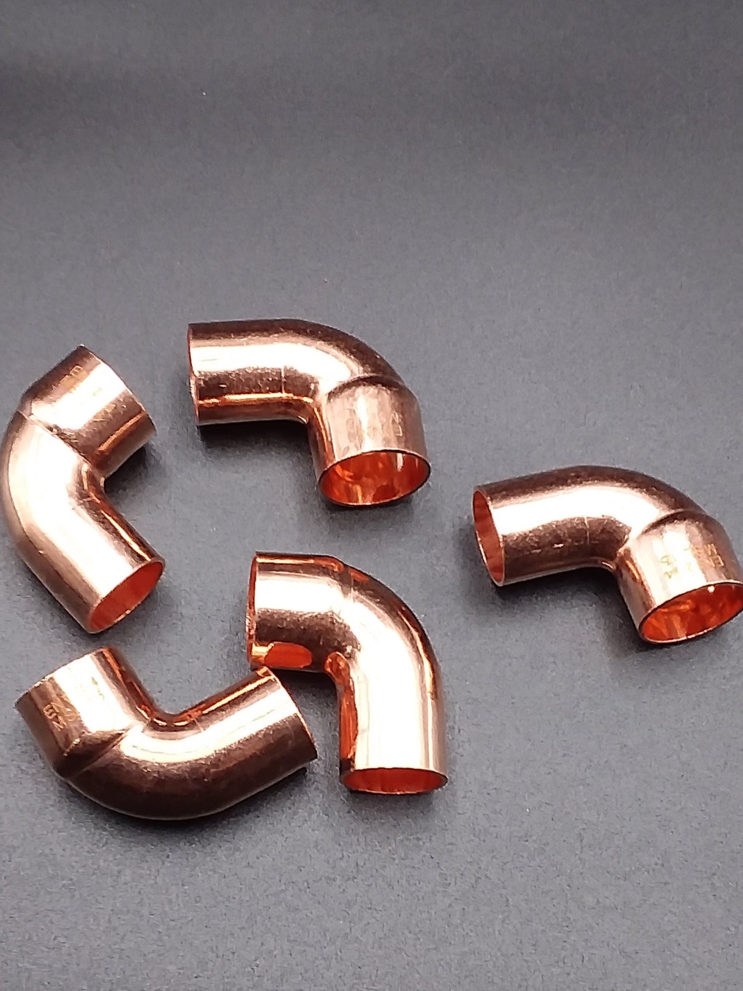 Copper end feed street elbows on a dark background.